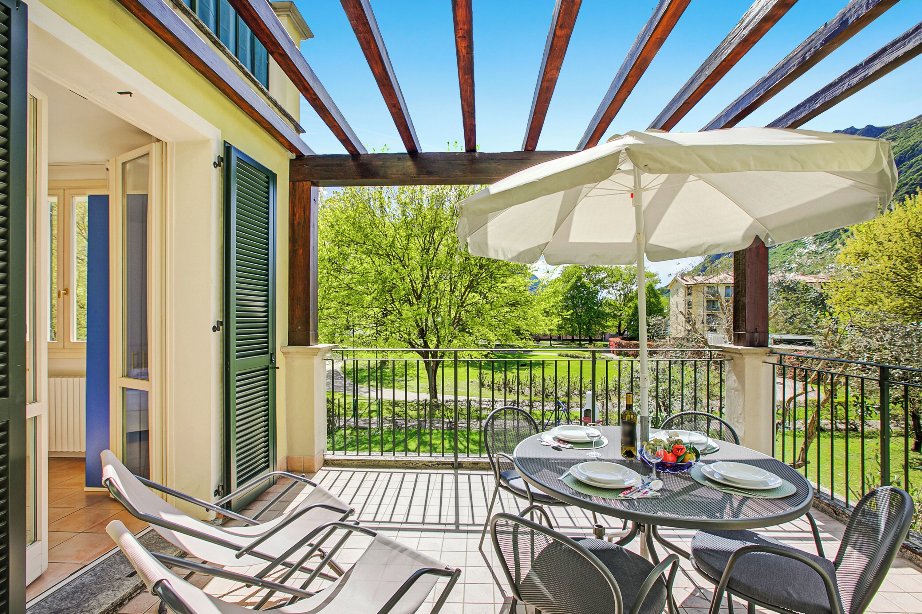 En overdækket terrasse med spisebord, stole og en stor parasol.