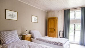 Ein Schlafzimmer mit zwei Betten, einer Holztür, einem Nachttisch mit Lampe und einem Fenster mit Vorhängen.