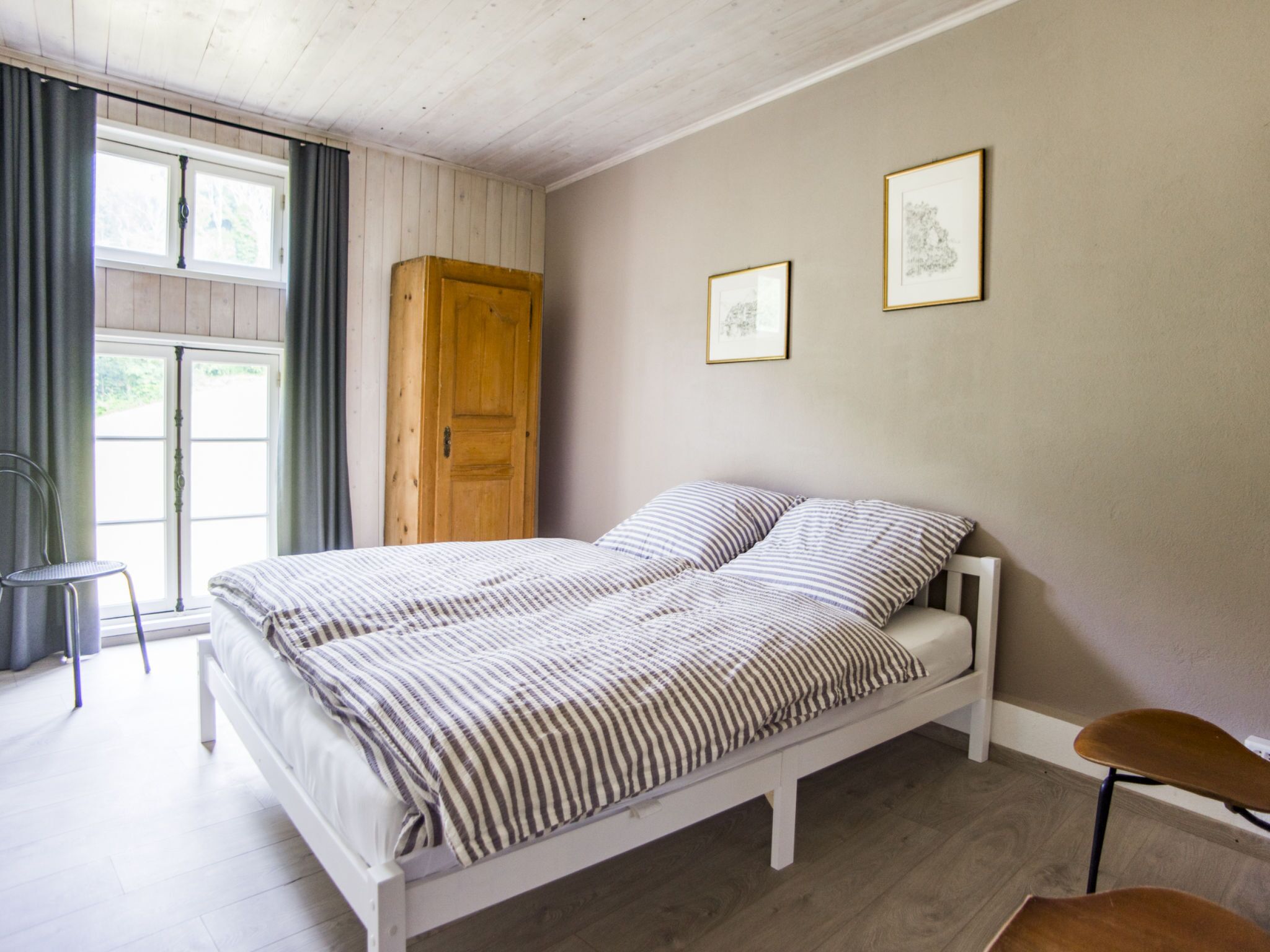 Ein Schlafzimmer mit einem Bett, einem Holzschrank, einem Sessel und zwei gerahmten Bildern an der Wand.