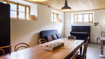 Ein Essbereich mit einem langen Holztisch, Stühlen, einem Klavier und einem großen Fenster.