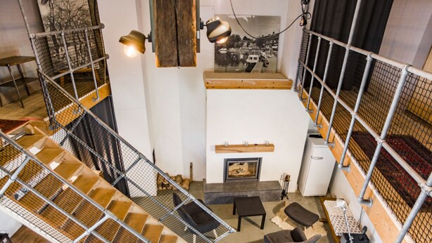 Ein mehrgeschossiges Interieur mit Treppe, Sitzgelegenheit, Kamin und einem Wandbild.
