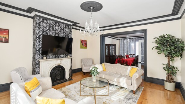 A living room with a fireplace, a television, a chandelier, and a dining area with a red tablecloth.