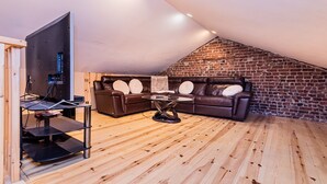 A loft-style room with a brick wall, a brown leather sofa, a wooden floor, and a TV on a stand.