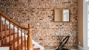 A staircase with wooden balusters leading to a landing with a glass table and a mirror on a brick wall.