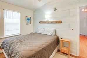 A bedroom with a bed, a bedside table, a wall-mounted lamp, and a window with blinds.