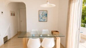 A dining area with a glass table and white chairs, a ceiling light, and a door leading to another room.