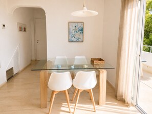 A dining area with a glass table and white chairs, a ceiling light, and a door leading to another room.