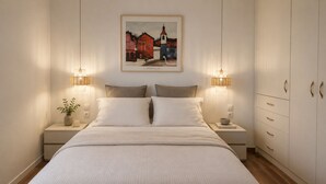 A bedroom with a bed, bedside tables, a nightstand with a plant, a framed picture on the wall, and a wardrobe with drawers.