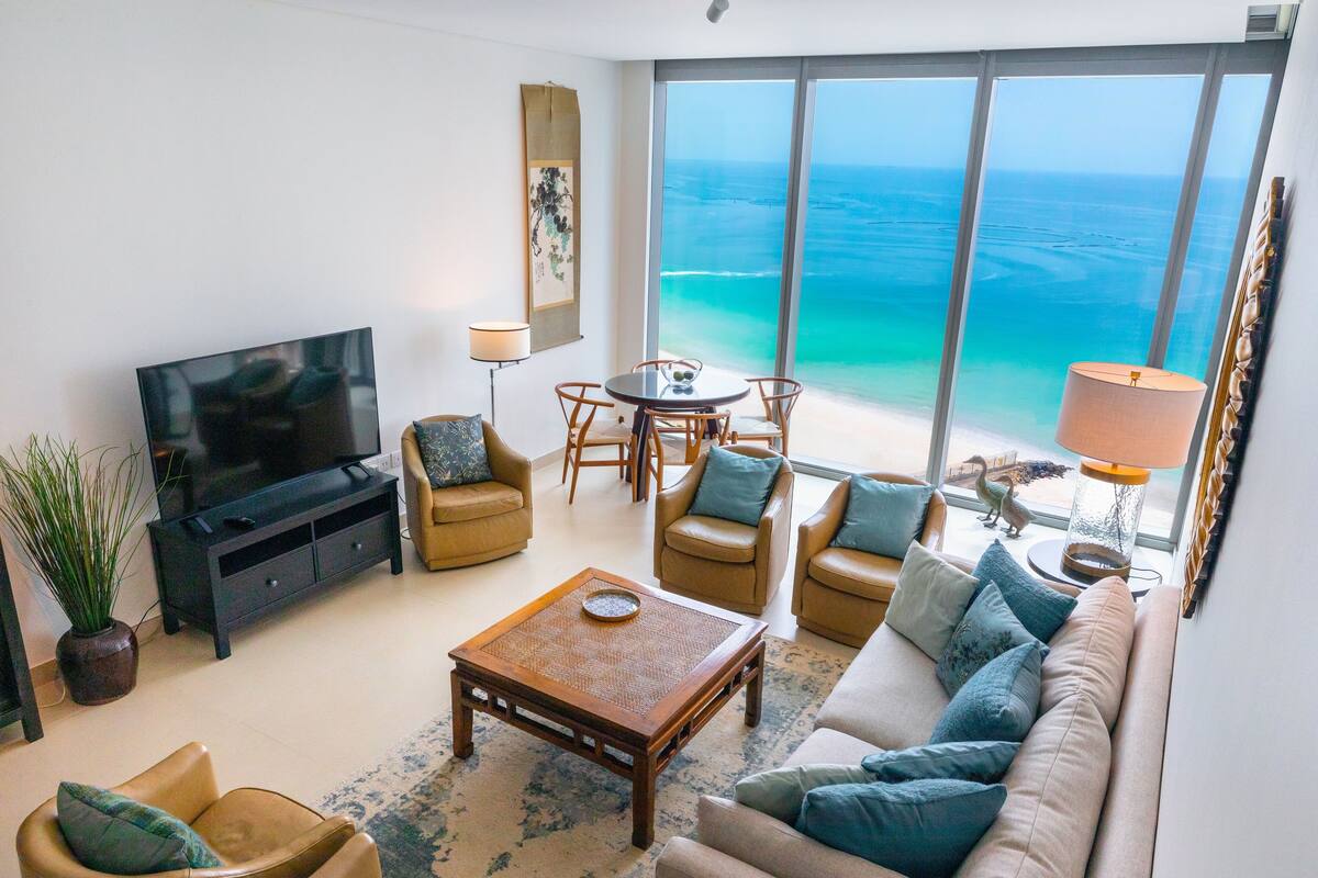 Een moderne woonkamer met een grote televisie, comfortabele zithoek, een eethoek en uitzicht op de oceaan.