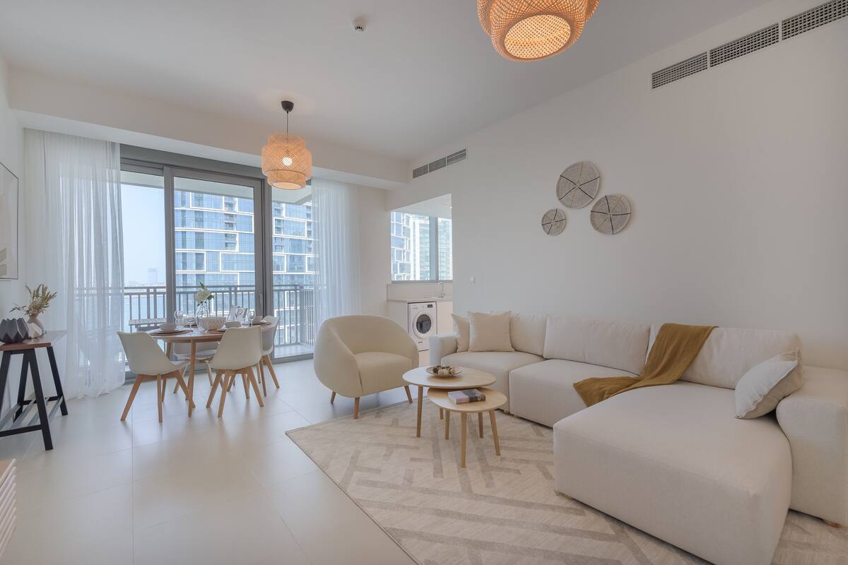 Een moderne woonkamer met een bank, eettafel, stoelen en een groot raam.