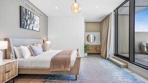 Ett modernt sovrum med en stor säng, sängbord, en hängande lampa, ett stort fönster och utsikt över omgivningarna.