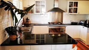 Et moderne køkken med hvide skabe, en sort bordplade og en central ø med to hvide stole.