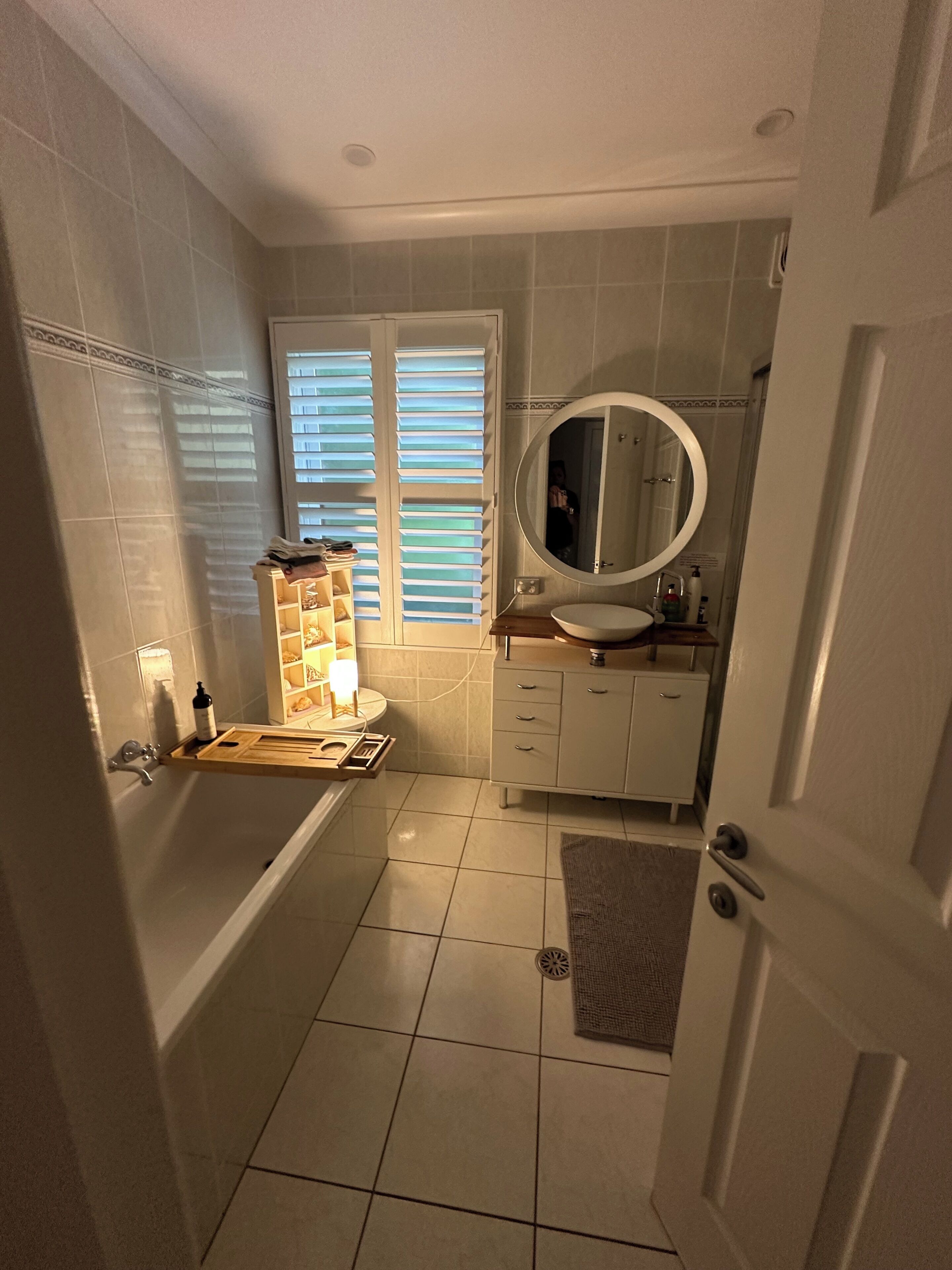 A bathroom with a bathtub, a sink, a mirror, and a window with blinds.