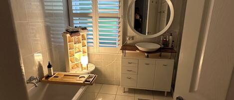 A bathroom with a bathtub, a sink, a mirror, and a window with blinds.
