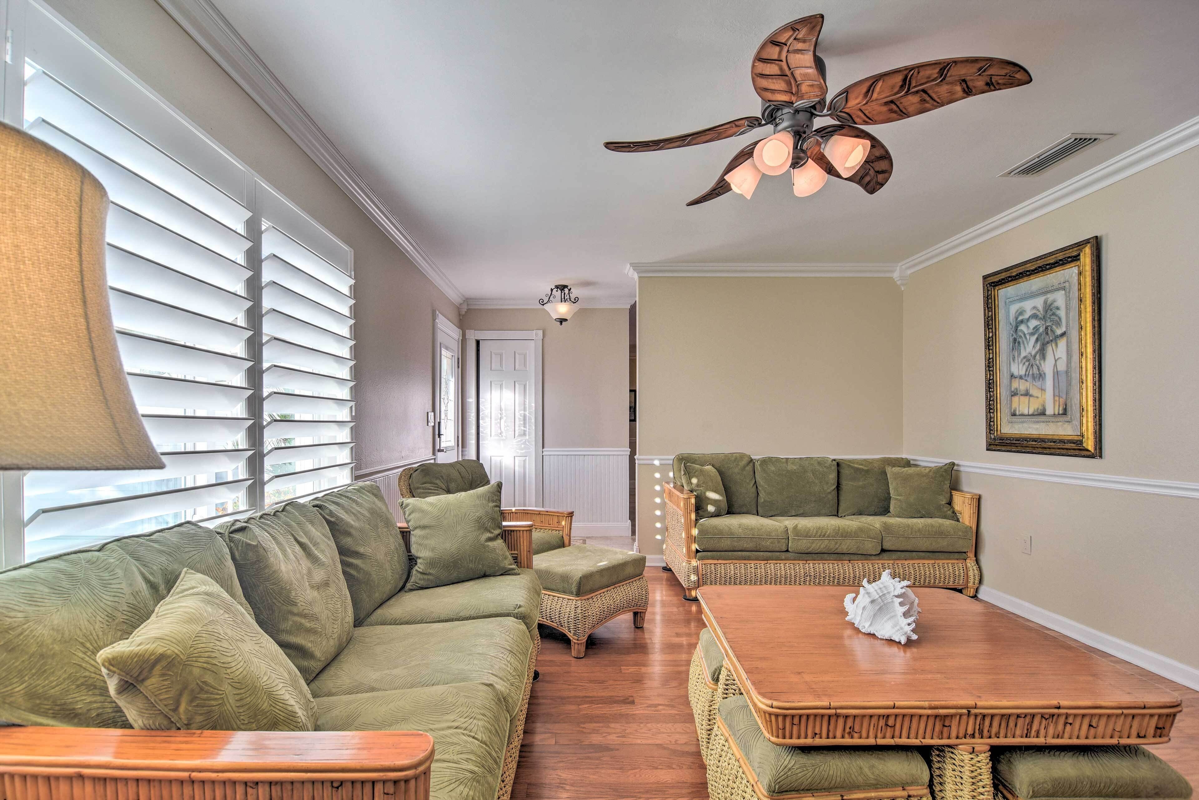 Ein Wohnzimmer mit einem grünen Sofa, Korbstühlen, einem Holztisch und einem Deckenventilator.