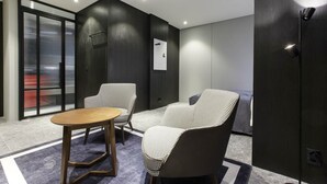 Una habitación moderna con una mesa redonda de madera, dos sillones con estampado, un sofá gris y un espejo grande.