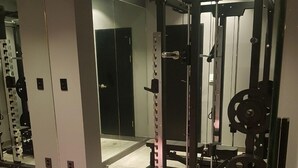 Un gimnasio con equipo de halterofilia, un espejo y una colchoneta rosa.