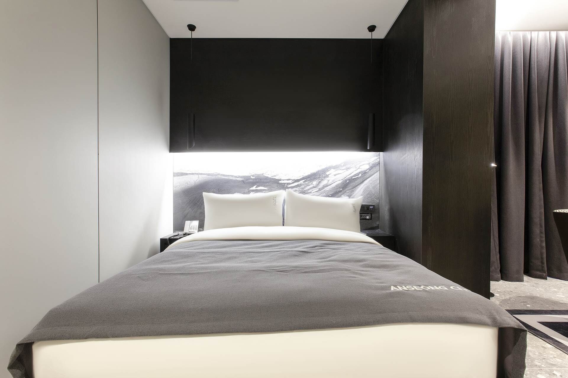 A modern hotel room with a bed, a nightstand, and a large window with a mountain view.