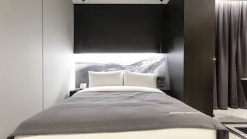 A modern hotel room with a bed, a nightstand, and a large window with a mountain view.