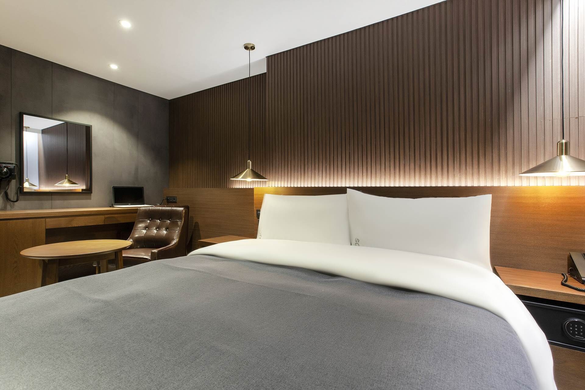 Una habitación de hotel moderna con una cama grande, un escritorio con silla, un espejo y dos lámparas colgantes.