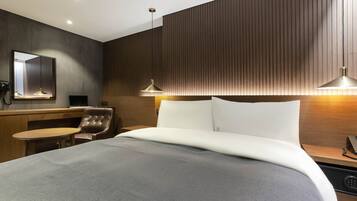 Una habitación de hotel moderna con una cama grande, un escritorio con silla, un espejo y dos lámparas colgantes.