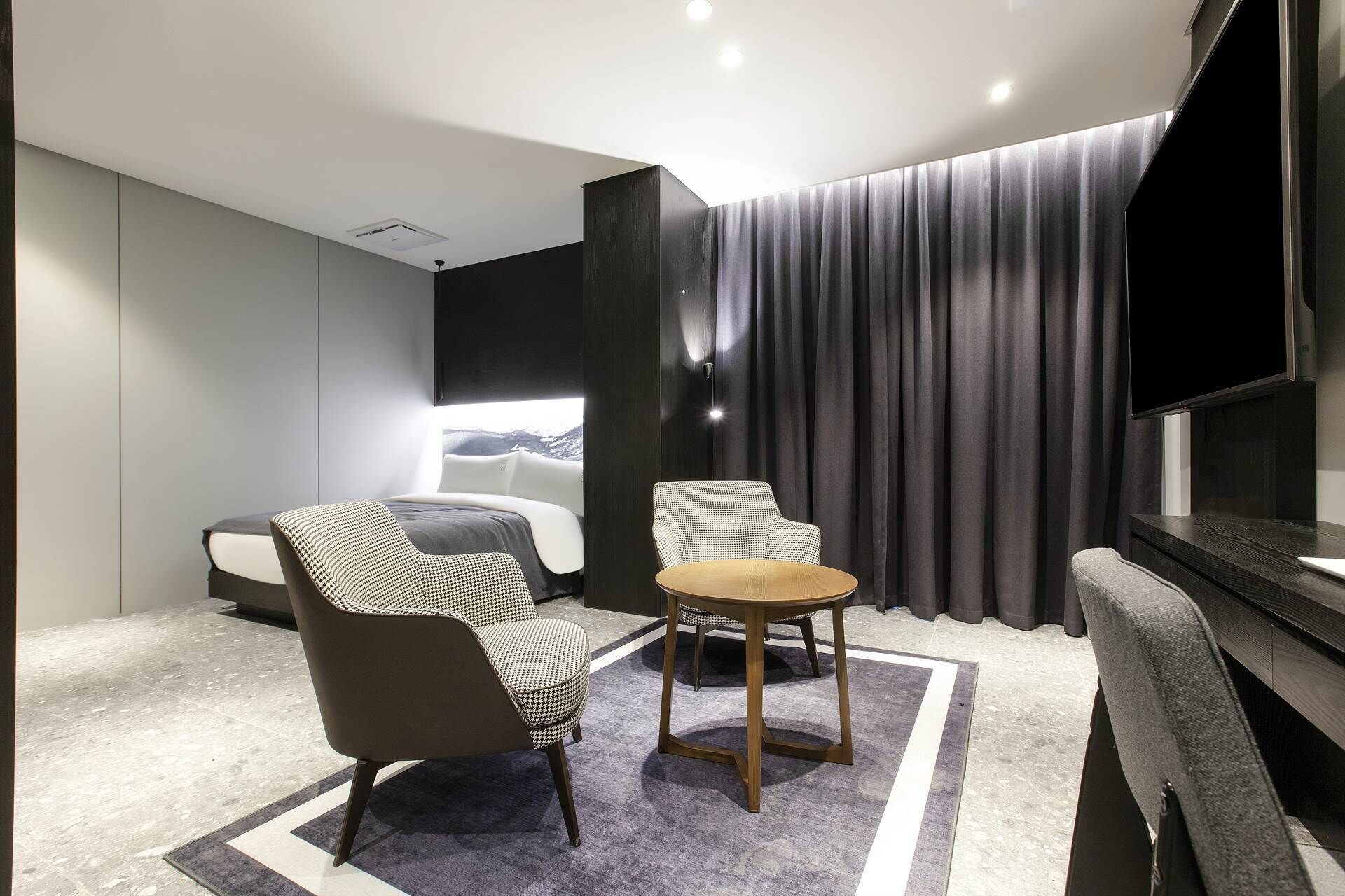 Une chambre d’hôtel moderne, équipée d’un lit, de deux fauteuils, d’une petite table ronde, d’un téléviseur à écran plat et offrant une vue sur un paysage enneigé par la fenêtre.