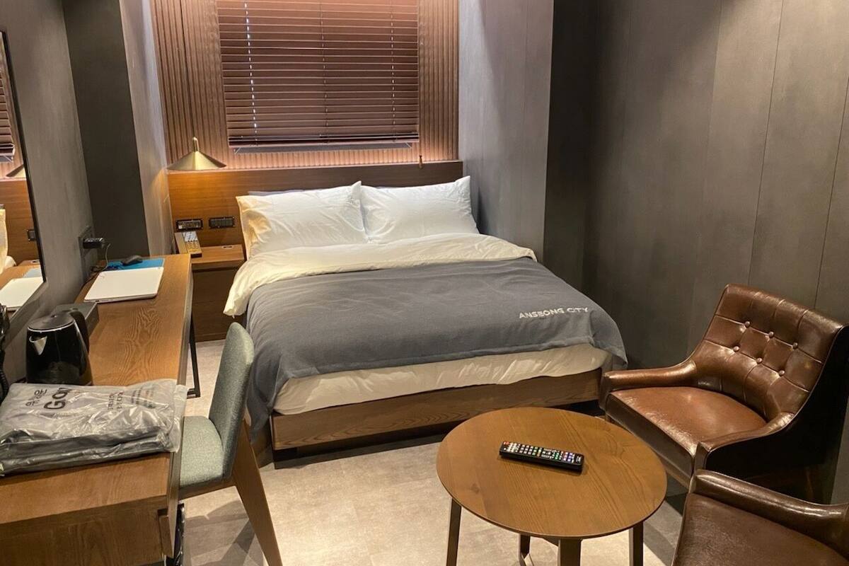 Una habitación de hotel con cama, escritorio con silla, una mesita redonda y un sillón de cuero.
