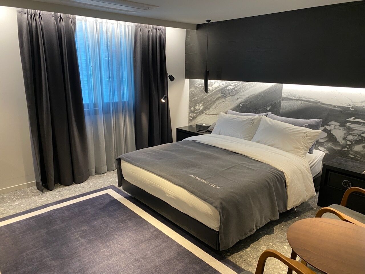 Hotellihuone, jossa on sänky, yöpöytä, työpöytä ja tuoli.