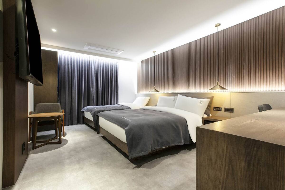 Una habitación de hotel moderna con dos camas, un escritorio, una silla y un televisor.