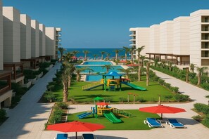 Relax by the central pool surrounded by lush greenery and palm trees, with ocean views and sun loungers for ultimate relaxation.