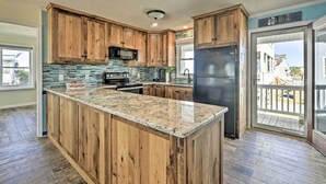 A kitchen with wooden cabinets, a granite countertop, a stainless steel refrigerator, and a large window. - Coastal Home: Walk to Holden Beach! (Holden Beach)