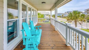 A covered porch with wooden flooring and white railings, featuring turquoise Adirondack chairs. - Coastal Home: Walk to Holden Beach! (Holden Beach)