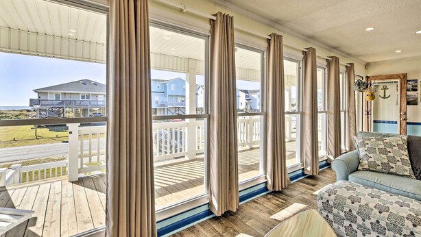 A room with large windows, a wooden deck, and a sofa with patterned cushions. - Coastal Home: Walk to Holden Beach! (Holden Beach)