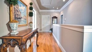 A hallway with wooden flooring, a white door, and a painting on the wall. - Trailside Manor - 0.5mi from UofA Campus! (Fayetteville)