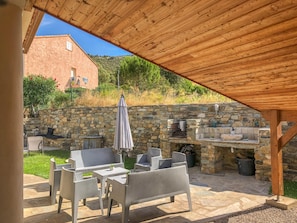 Um pátio ao ar livre com paredes de pedra, uma pérgola de madeira e uma lareira de pedra.