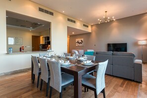 A modern living room with a dining area, a gray sofa, a flat-screen TV, and a chandelier. - EDEN'S Homes & Villas - Dream Palm Residences (Dubai)