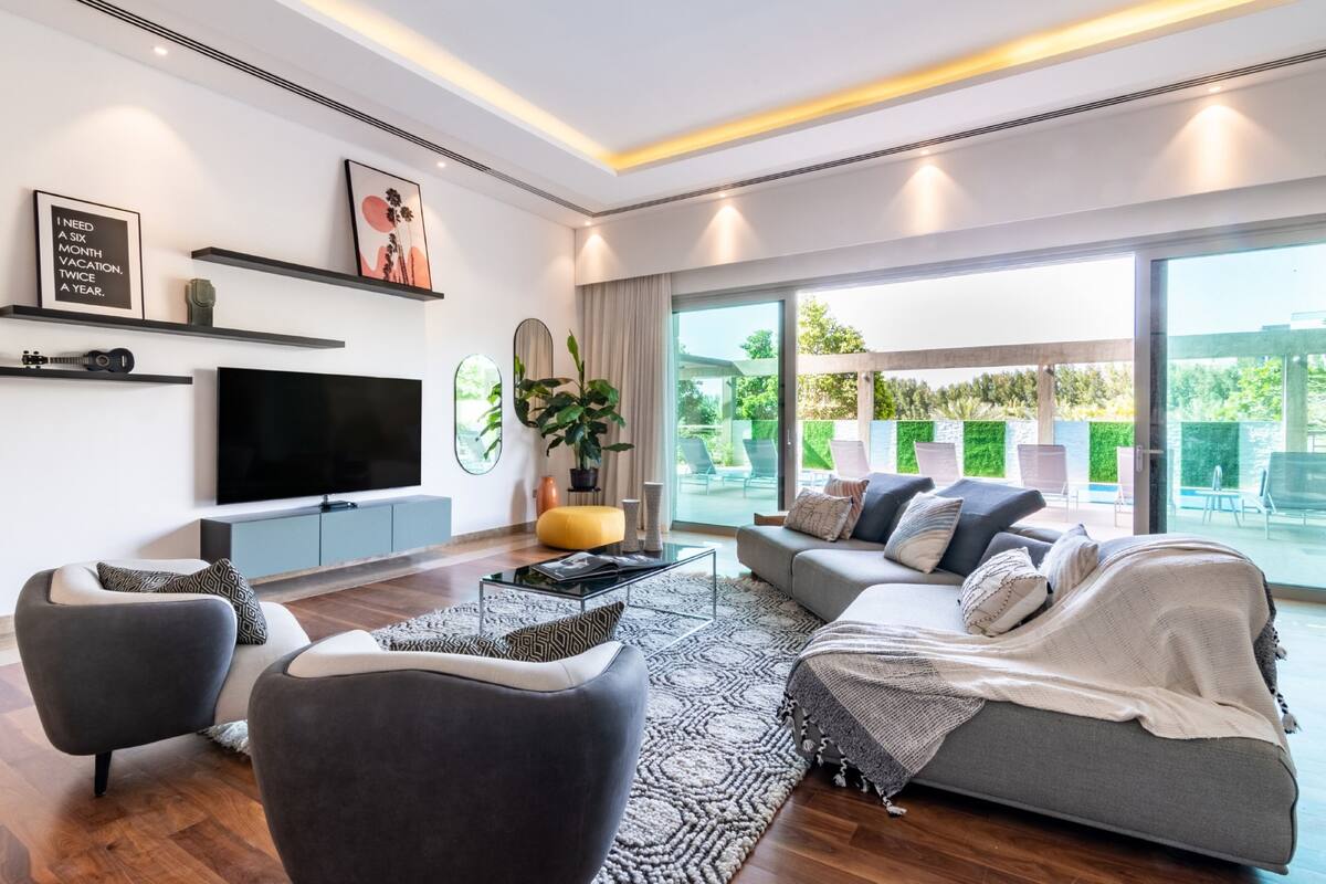 Una sala de estar moderna con un televisor de pantalla plana grande, asientos cómodos y un amplio ventanal con vistas al exterior.