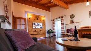 Ein gemütliches Wohnzimmer mit einer Couch, einem runden Tisch mit Flasche und Glas, einem Kamin und einem an der Wand befestigten Fernseher.