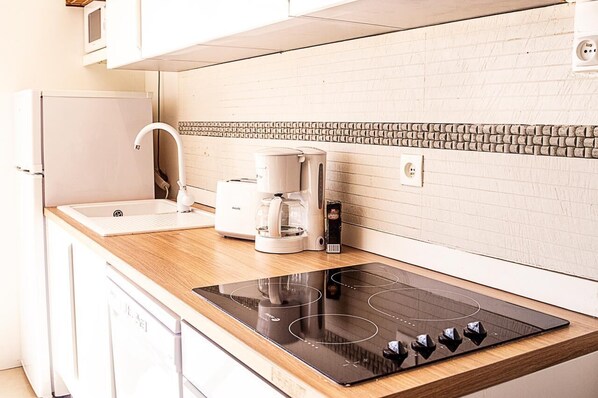A modern kitchen with a built-in induction cooktop, a coffee maker, and a refrigerator.