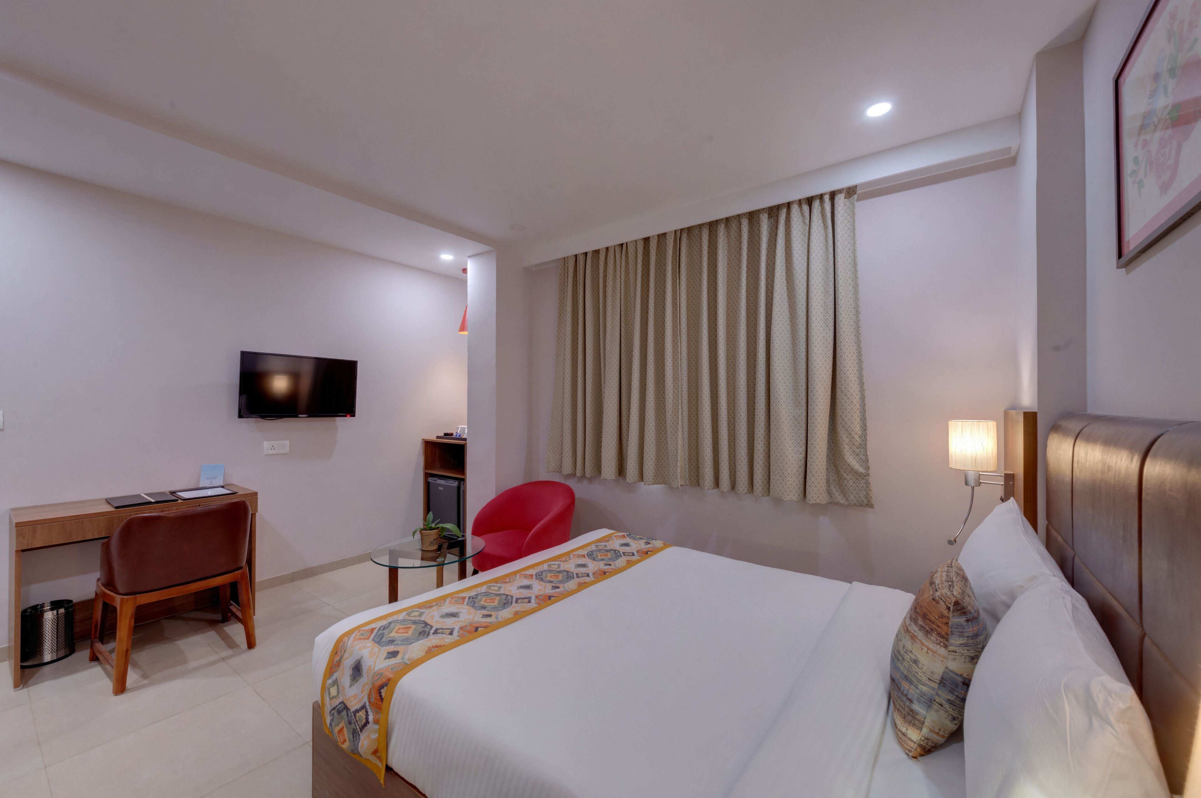 Habitación de hotel con cama, escritorio, silla, televisor y ventana con cortinas.