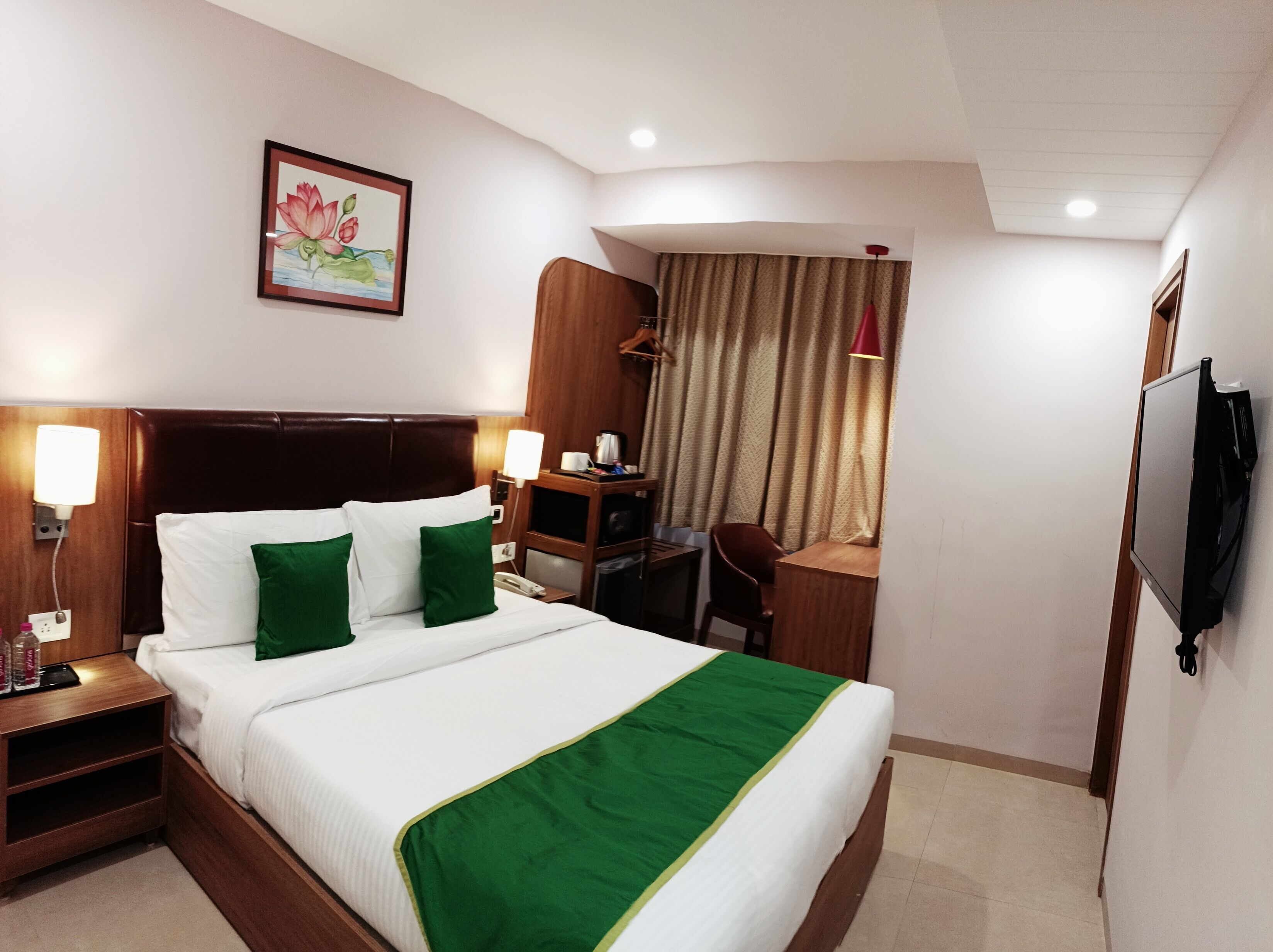A hotel room with a large bed, a desk, a chair, a TV, and a painting on the wall.