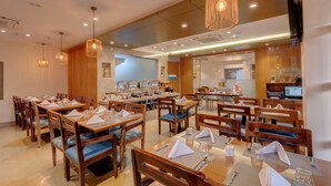 A restaurant with wooden tables and chairs, a buffet area, and a kitchen visible in the background. - The Beacon Hotel Vadodara (Vadodara)