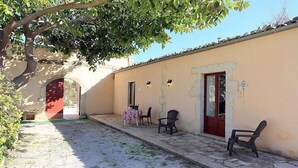 A courtyard with a table and chairs, a red door, and a tree providing shade.