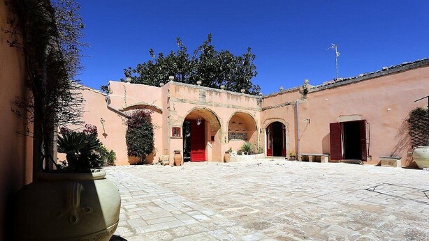 A courtyard with a central archway, potted plants, and a large urn.