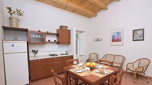 A compact kitchen with wooden cabinets, a white refrigerator, and a dining table set for four with wicker chairs.