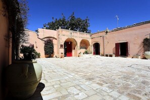 A courtyard with a central archway, potted plants, and a large urn.