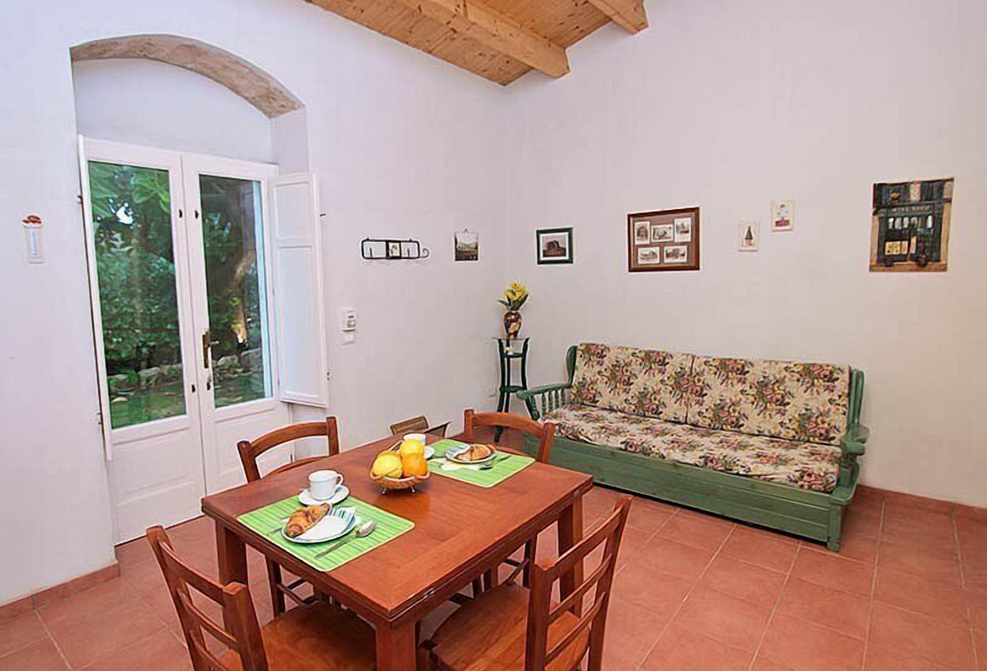 A dining area with a wooden table and chairs, a floral sofa, and a wall with framed pictures.