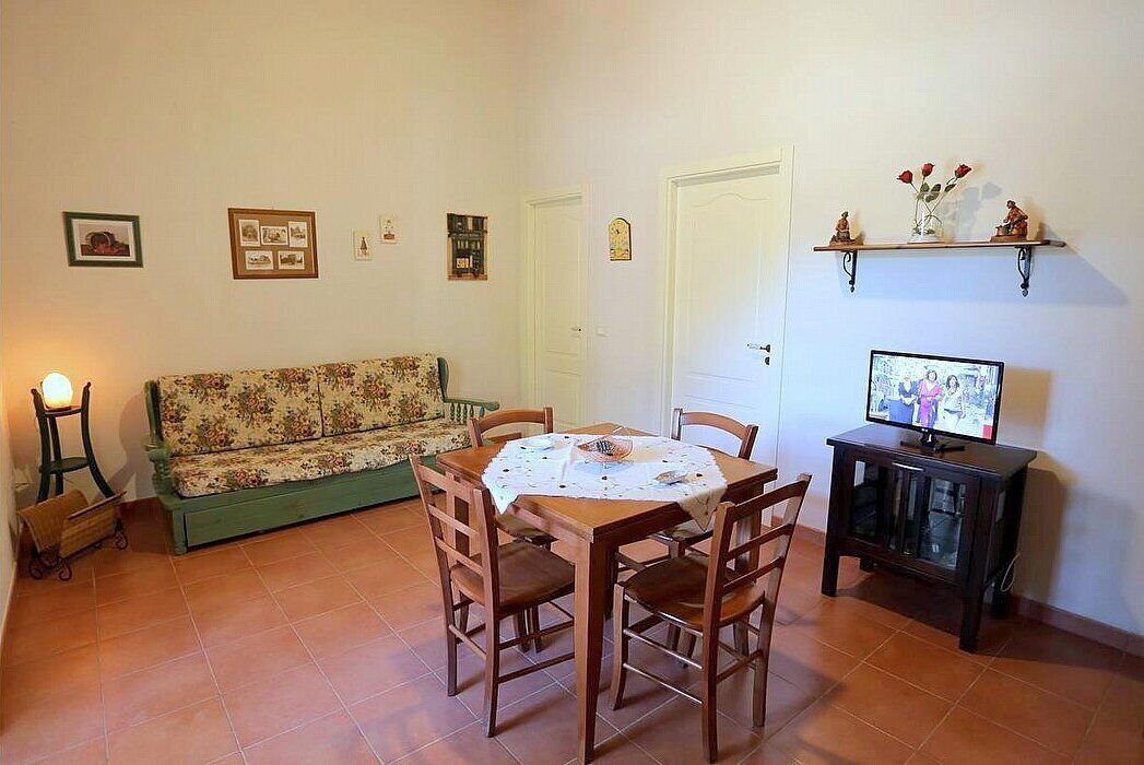 A cozy living room with a floral sofa, a wooden dining table with chairs, a television on a cabinet, and a small cabinet with a TV.