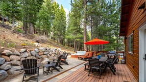 A deck with outdoor furniture, a stone wall, and a wooden building. - Pet-Friendly Escape | Hot Tub, King Suite, Rec Center Access | Near Lake, Trails (Truckee)