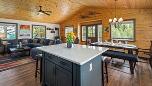 A spacious living area with a wooden ceiling, a sofa set, a dining table with chairs, and a kitchen island. - Pet-Friendly Escape | Hot Tub, King Suite, Rec Center Access | Near Lake, Trails (Truckee)